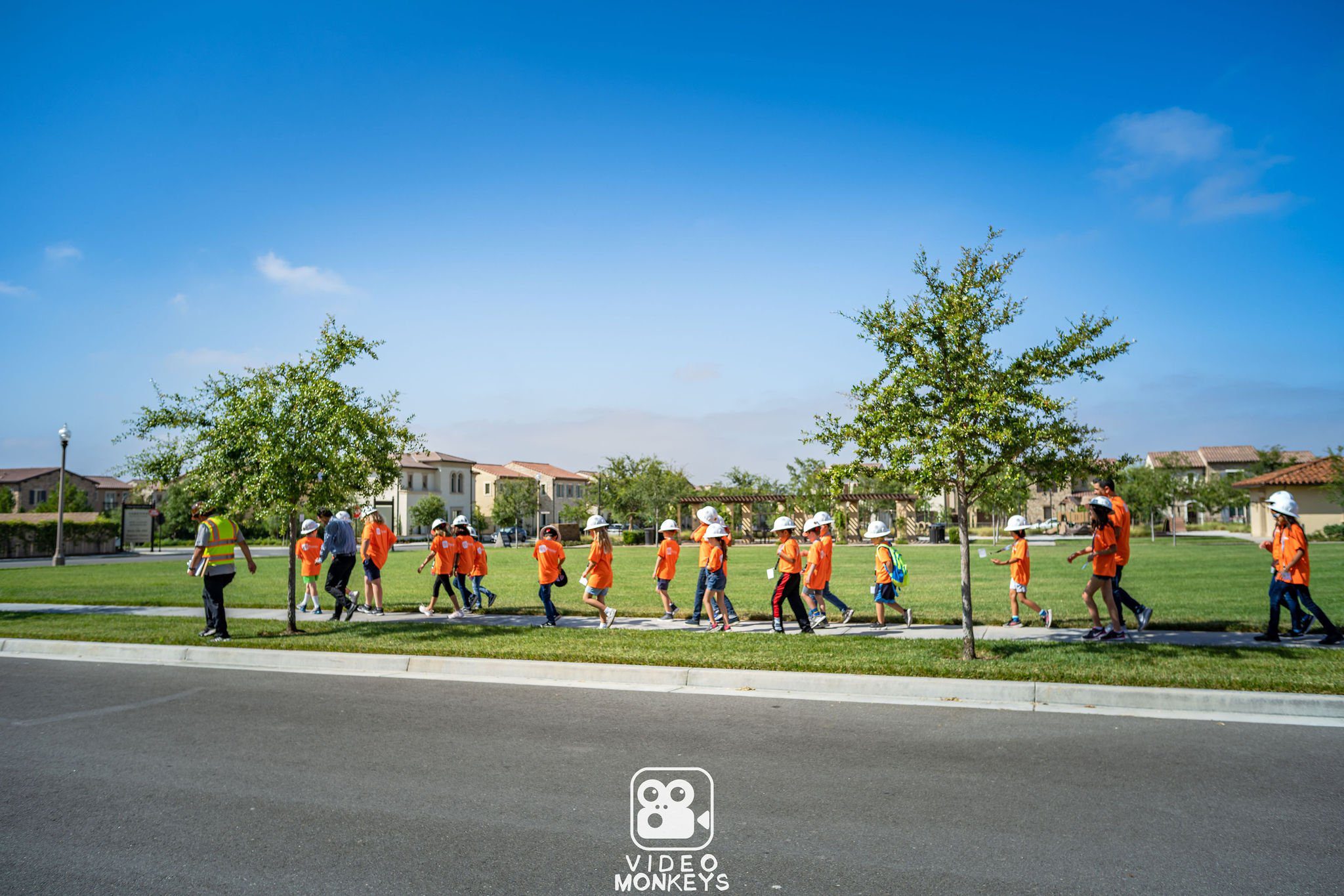 Children in orange shirts and hard hats walking with adults.