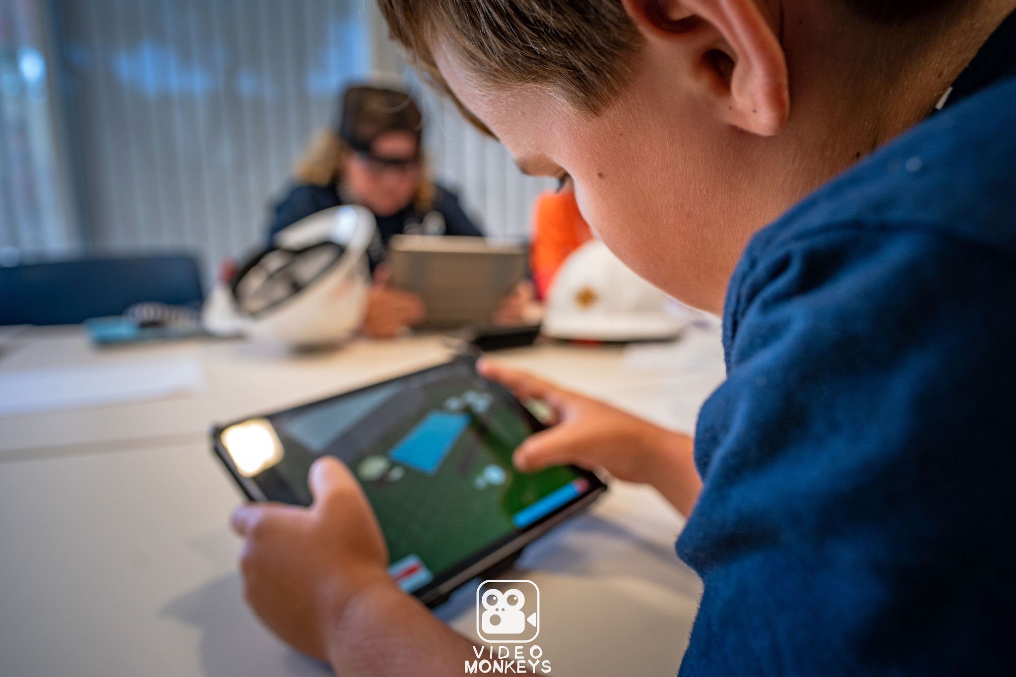 Close-up of a child playing a game on a tablet, with other children in the background during a workshop.