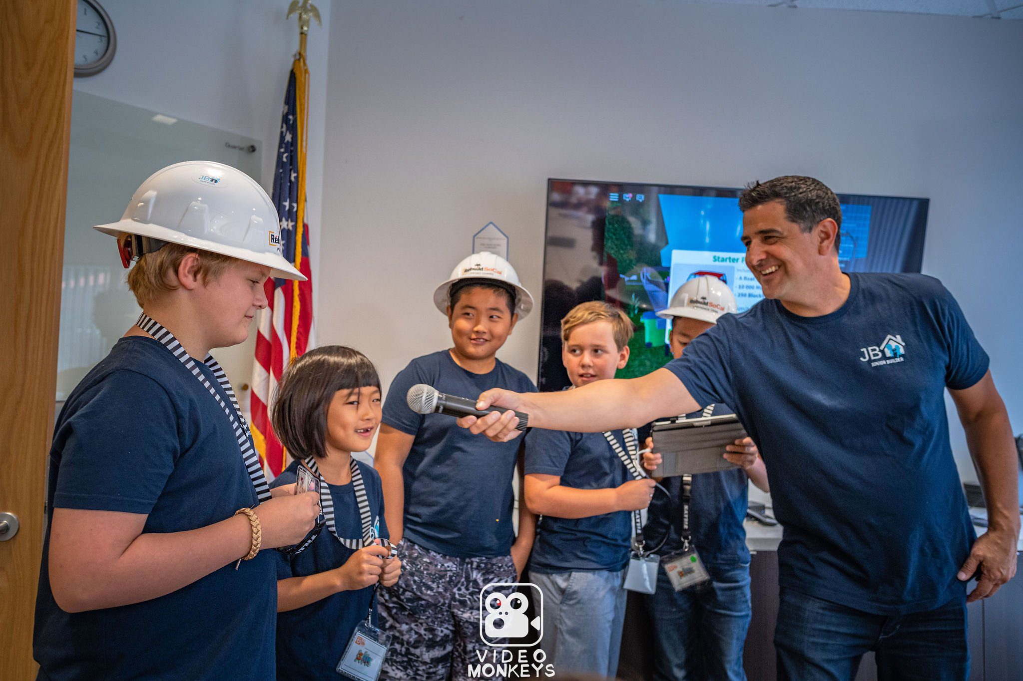 Junior Builder graduation ceremony with children wearing hard hats and badges.