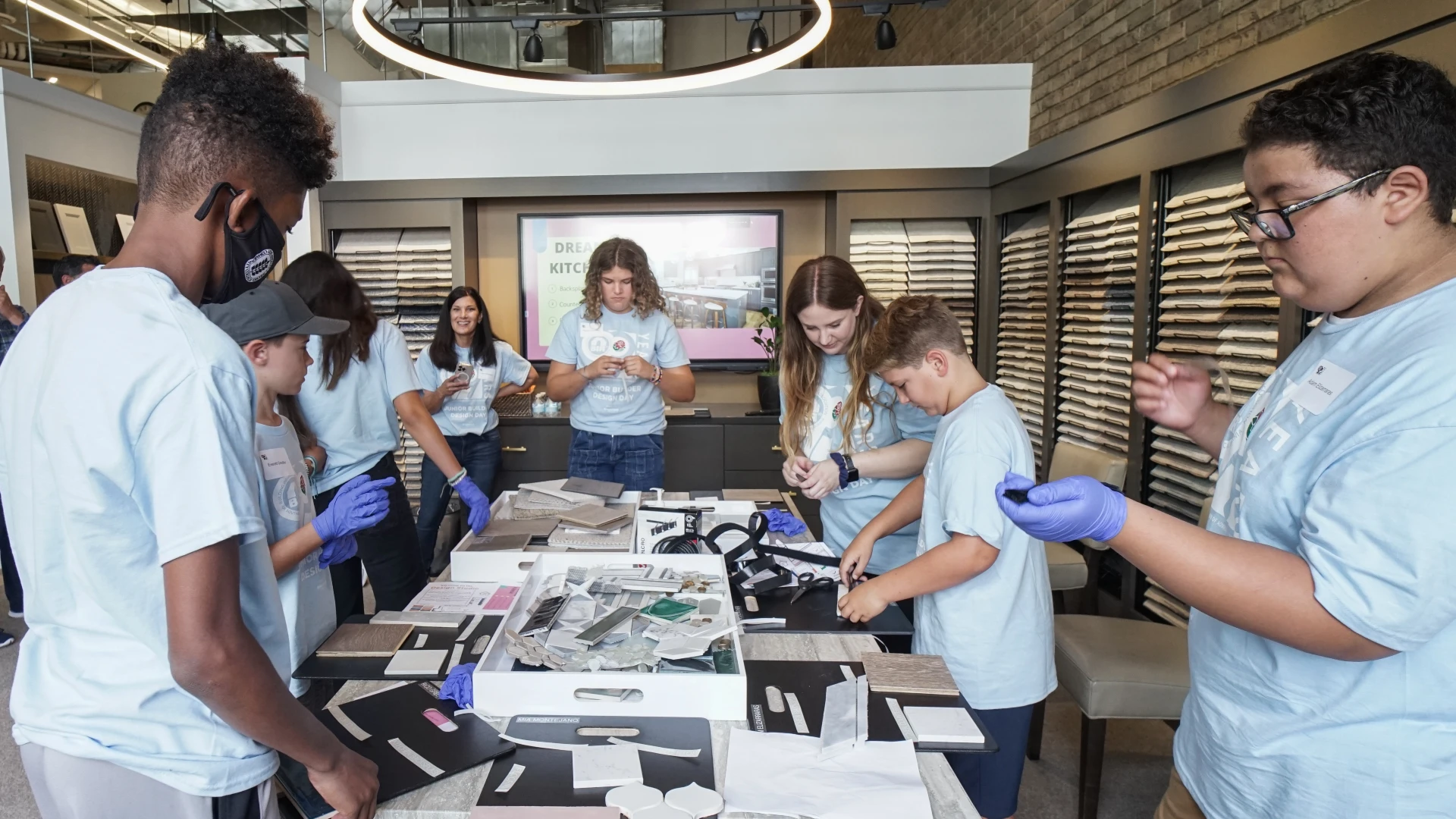 Students in blue t-shirts participating in a hands-on design workshop, working with materials in a modern showroom.